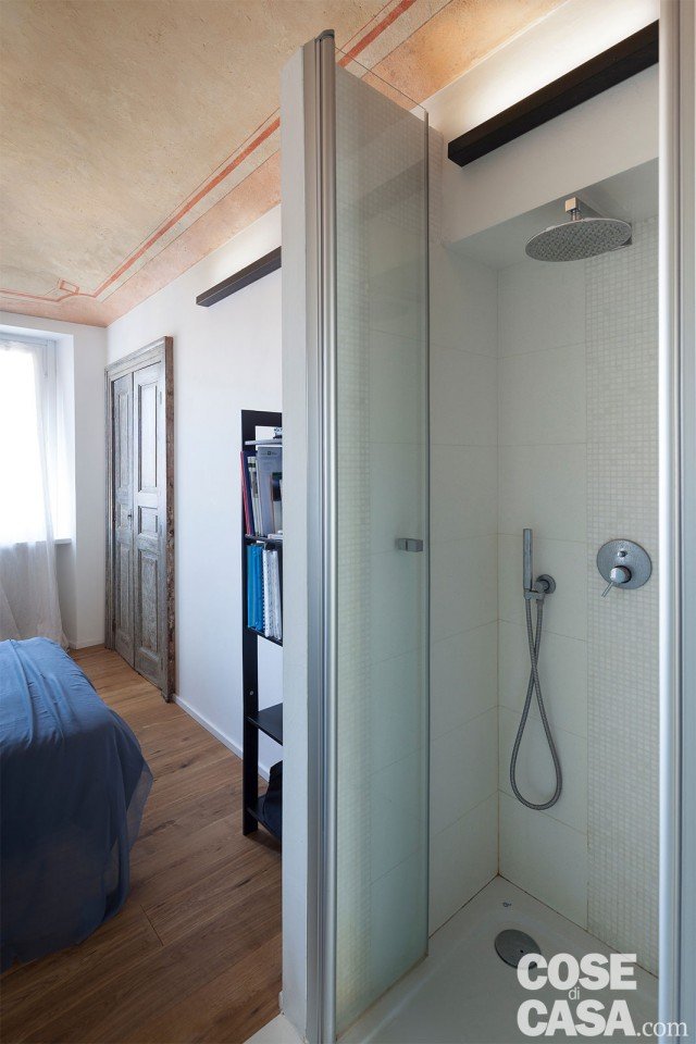 La doccia in muratura non arriva a tutta altezza per lasciare filtrare la luce naturale all’interno del box, rivestito in gres porcellanato e mosaico. Sulla parete di fronte al letto, una porta di recupero chiude un armadio a muro. La doccia in muratura non arriva a tutta altezza per lasciare filtrare la luce naturale all’interno del box, rivestito in gres porcellanato e mosaico. Sulla parete di fronte al letto, una porta di recupero chiude un armadio a muro.