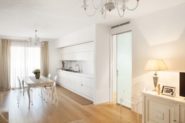Il living di questo appartamento è una sorta di stile neoromantico, ottenuto mixando due stili: minimalista, per la scelta di porte filomuro, dalle linee contemporanee e squadrate, e della cucina total white come le pareti, e classico, per la presenza di arredi come il tavolo, la madia bugnata e i lampadari a bracci con paralume. Il living di questo appartamento è una sorta di stile neoromantico, ottenuto mixando due stili: minimalista, per la scelta di porte filomuro, dalle linee contemporanee e squadrate, e della cucina total white come le pareti, e classico, per la presenza di arredi come il tavolo, la madia bugnata e i lampadari a bracci con paralume.