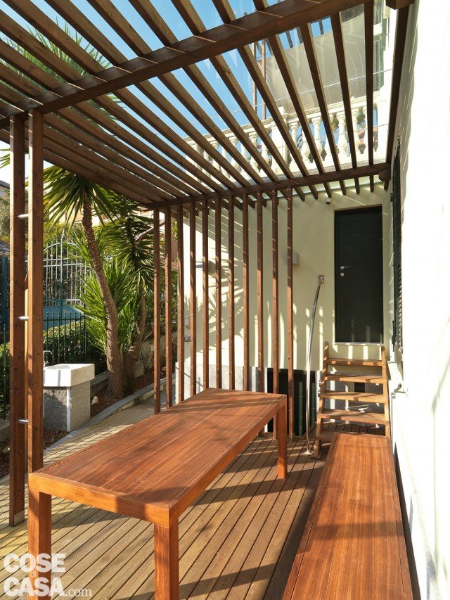 Davanti all’ingresso è stato realizzato un porticato con una tettoia formata da sottili listelli di legno. La fascia a pavimento è rivestita con assi di teak in finitura naturale. Questo spazio ombreggiato, sviluppato in lunghezza, è stato utilizzato per ricavare una zona pranzo all’aperto. Davanti all’ingresso è stato realizzato un porticato con una tettoia formata da sottili listelli di legno. La fascia a pavimento è rivestita con assi di teak in finitura naturale. Questo spazio ombreggiato, sviluppato in lunghezza, è stato utilizzato per ricavare una zona pranzo all’aperto.