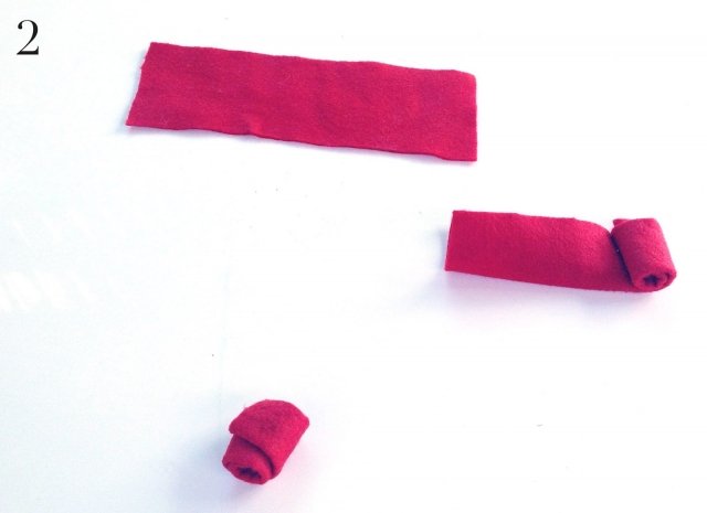 1) Ritagliare un rettangolo di tessuto rosso (pannolenci) di circa 15 x 15cm. Piegare il rettangolo di tessuto in due dal lato più lungo, quindi dalla parte più corta iniziare ad avvolgerlo fino ad ottenere il fiore che verrà bloccato con un tocco di colla a caldo. 1) Ritagliare un rettangolo di tessuto rosso (pannolenci) di circa 15 x 15cm. Piegare il rettangolo di tessuto in due dal lato più lungo, quindi dalla parte più corta iniziare ad avvolgerlo fino ad ottenere il fiore che verrà bloccato con un tocco di colla a caldo.