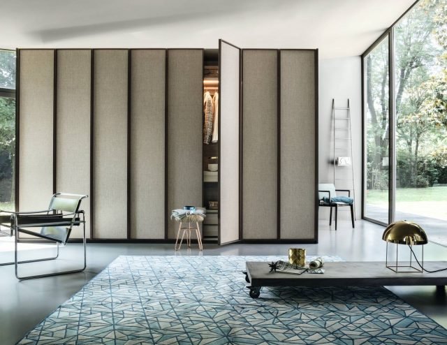 Materiali ricercati e aspetto contemporaneo distinguono l’armadio Dandy (Officinadesign Lema), con ante a battente dal frame perimetrale in metallo verniciato bronzo. I pannelli hanno un raffinato rivestimento decorativo tessile, ma sono disponibili anche in vetro trasparente o serigrafato dall’elegante effetto garzato, che richiama lo stile orientale. Gli interni – in questo caso larice grigio – offrono svariati accessori organizzativi, tra cui scarpiera in vetro con luce incorporata, teca con top in vetro e vassoio estraibile a scomparti in ecopelle, ripiani in vetro. Materiali ricercati e aspetto contemporaneo distinguono l’armadio Dandy (Officinadesign Lema), con ante a battente dal frame perimetrale in metallo verniciato bronzo. I pannelli hanno un raffinato rivestimento decorativo tessile, ma sono disponibili anche in vetro trasparente o serigrafato dall’elegante effetto garzato, che richiama lo stile orientale. Gli interni – in questo caso larice grigio – offrono svariati accessori organizzativi, tra cui scarpiera in vetro con luce incorporata, teca con top in vetro e vassoio estraibile a scomparti in ecopelle, ripiani in vetro.