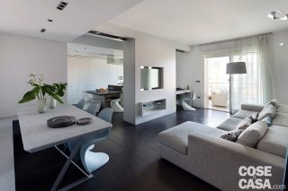 Soggiorno con divano grigio, tavolo e cucina dietro una colonna