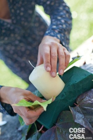 Posizionare la spugna nel sottovaso, tagliare i 4 angoli in obliquo. Mettere la candela al centro, facendola entrare nella spugna per circa 2-3 cm. Inserire il picciolo delle foglie più grosse tutto intorno alla base della spugna e poi fare un secondo giro nella parte alta, attorno alla candela, con le foglie più piccole. Mantenete una forma circolare attorno alla candela. Posizionare la spugna nel sottovaso, tagliare i 4 angoli in obliquo. Mettere la candela al centro, facendola entrare nella spugna per circa 2-3 cm. Inserire il picciolo delle foglie più grosse tutto intorno alla base della spugna e poi fare un secondo giro nella parte alta, attorno alla candela, con le foglie più piccole. Mantenete una forma circolare attorno alla candela.