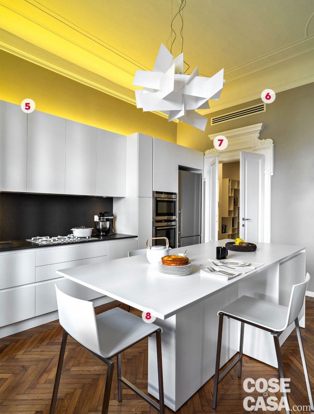 5. Luce gialla in alto Sopra la composizione della cucina, che raggiunge con colonne e pensili l'altezza dello stipite della porta, è stato installato su tutta la lunghezza uno strip led: produce una luce diffusa e calda, di tonalità tendente al giallo. Dal basso verso l'alto, un'illuminazione indiretta e morbida che "abbraccia" l'ambiente nel suo insieme. 6. La climatizzazione è canalizzata I ribassamenti del soffitto di ingresso e corridoio hanno anche la funzione di alloggiare gli elementi dell'impianto di raffrescamento canalizzato. Sono installate un'unità motocondensante interna e una esterna sul balconcino del pianerottolo; le griglie di erogazione dell'aria sono posizionate nei diversi ambienti, nella fascia alta delle pareti. Per il riscaldamento è stato invece mantenuto l'impianto tradizionale con i radiatori in ghisa. 7. Il decoro sopra la porta In cucina, completa la parte superiore dello stipite. In legno smaltato bianco, con leggero contrasto sullo sfondo grigio della parete, è stato realizzato con lavorazione manuale da artigiani alpini. 8. Controsoffitti & contropareti Poiché la ristrutturazione ha comportato importanti opere impiantistiche in cucina e nei bagni, i ribassamenti a soffitto di circa 40 cm nelle zone di passaggio e anche le contropareti del corridoio sono stati realizzati con la funzione tecnica fondamentale di alloggiare i cavi elettrici e i condotti idraulici. La profondità creata dalle contropareti è stata inoltre sfruttata per ricavare delle nicchie e per inserire i moduli della libreria a giorno riducendone l'ingombro. 5. Luce gialla in alto Sopra la composizione della cucina, che raggiunge con colonne e pensili l'altezza dello stipite della porta, è stato installato su tutta la lunghezza uno strip led: produce una luce diffusa e calda, di tonalità tendente al giallo. Dal basso verso l'alto, un'illuminazione indiretta e morbida che "abbraccia" l'ambiente nel suo insieme. 6. La climatizzazione è canalizzata I ribassamenti del soffitto di ingresso e corridoio hanno anche la funzione di alloggiare gli elementi dell'impianto di raffrescamento canalizzato. Sono installate un'unità motocondensante interna e una esterna sul balconcino del pianerottolo; le griglie di erogazione dell'aria sono posizionate nei diversi ambienti, nella fascia alta delle pareti. Per il riscaldamento è stato invece mantenuto l'impianto tradizionale con i radiatori in ghisa. 7. Il decoro sopra la porta In cucina, completa la parte superiore dello stipite. In legno smaltato bianco, con leggero contrasto sullo sfondo grigio della parete, è stato realizzato con lavorazione manuale da artigiani alpini. 8. Controsoffitti & contropareti Poiché la ristrutturazione ha comportato importanti opere impiantistiche in cucina e nei bagni, i ribassamenti a soffitto di circa 40 cm nelle zone di passaggio e anche le contropareti del corridoio sono stati realizzati con la funzione tecnica fondamentale di alloggiare i cavi elettrici e i condotti idraulici. La profondità creata dalle contropareti è stata inoltre sfruttata per ricavare delle nicchie e per inserire i moduli della libreria a giorno riducendone l'ingombro.