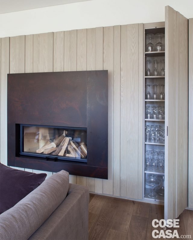 La boiserie/contenitore: addossato alla parete di spina e centrale rispetto alle due aperture, un pannello decorativo in legno cela una serie di moduli contenitori. Solo in corrispondenza del camino, incassato nel muro a un terzo della sua estensione, si tratta effettivamente di un tamponamento, che nasconde la parte tecnica del focolare. È, infatti, di un mobile realizzato in nobilitato, profondità 27 cm, con ante doppiamente rivestite all’esterno con doghe di rovere rigatino di diverso spessore e larghezza. Questa duplice e alternata impiallacciatura dà vita alla scansione tridimensionale che caratterizza l’estetica della parete. E che la rende assolutamente unica. In più, mimetizza la modularità irregolare delle aperture e dei vani retrostanti corrispondenti. La boiserie/contenitore: addossato alla parete di spina e centrale rispetto alle due aperture, un pannello decorativo in legno cela una serie di moduli contenitori. Solo in corrispondenza del camino, incassato nel muro a un terzo della sua estensione, si tratta effettivamente di un tamponamento, che nasconde la parte tecnica del focolare. È, infatti, di un mobile realizzato in nobilitato, profondità 27 cm, con ante doppiamente rivestite all’esterno con doghe di rovere rigatino di diverso spessore e larghezza. Questa duplice e alternata impiallacciatura dà vita alla scansione tridimensionale che caratterizza l’estetica della parete. E che la rende assolutamente unica. In più, mimetizza la modularità irregolare delle aperture e dei vani retrostanti corrispondenti.