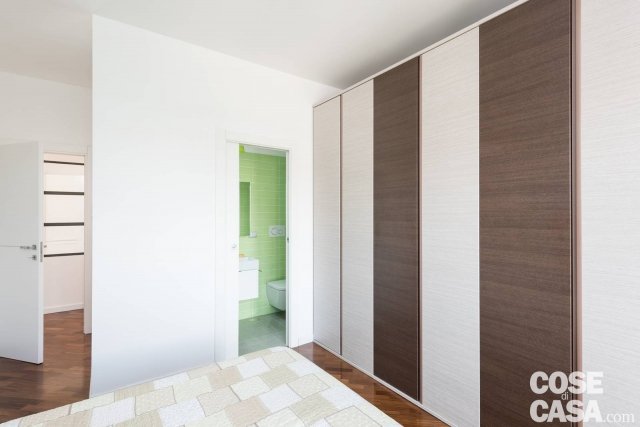 La camera da letto, posizionata sul fondo dell’appartamento e dotata di piccolo bagno privato, è caratterizzata da una grande armadiatura Colombini con ante scorrevoli dalla finitura venata del legno alternato sbiancato e naturale scuro. Una soluzione ad alto contenimento per l’organizzazione degli abiti, che quasi si mimetizza nelle strutture murarie verticali, trasformandosi in semplice segno grafico. Unico tocco cromatico deciso quello del rivestimento ceramico del bagno, che si intravede quando la porta è aperta. Il parquet preesistente è stato mantenuto anche nella zona notte, per dare continuità percettiva e ampliare spazialmente la superficie a disposizione. La camera da letto, posizionata sul fondo dell’appartamento e dotata di piccolo bagno privato, è caratterizzata da una grande armadiatura Colombini con ante scorrevoli dalla finitura venata del legno alternato sbiancato e naturale scuro. Una soluzione ad alto contenimento per l’organizzazione degli abiti, che quasi si mimetizza nelle strutture murarie verticali, trasformandosi in semplice segno grafico. Unico tocco cromatico deciso quello del rivestimento ceramico del bagno, che si intravede quando la porta è aperta. Il parquet preesistente è stato mantenuto anche nella zona notte, per dare continuità percettiva e ampliare spazialmente la superficie a disposizione.