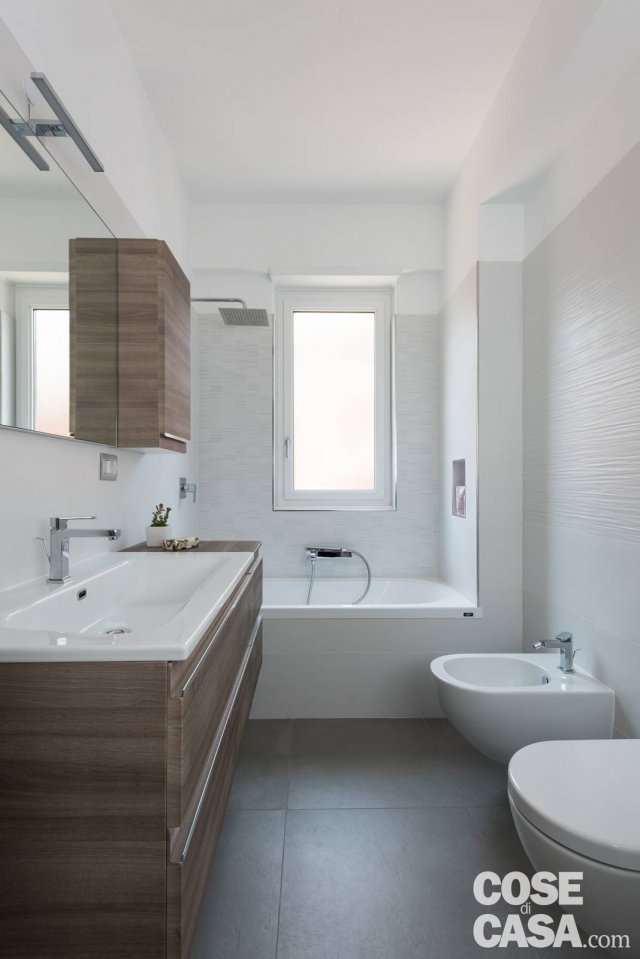 Più sobrio e maschile il bagno principale, declinato nei toni sobri del bianco e del grigio dei rivestimenti ABK a pavimento e a parete, a cui fa da contrappunto il calore del legno scelto per il mobile contenitore sotto il lavabo e il pensile. Il posizionamento della vasca sul fondo del locale, sotto alla finestra, è una soluzione che permette di ampliare la percezione visiva dell’ambiente e nel contempo liberare la superficie disponibile, per un più agevole utilizzo dei sanitari Catalano dotati di rubinetterie Nobili. Più sobrio e maschile il bagno principale, declinato nei toni sobri del bianco e del grigio dei rivestimenti ABK a pavimento e a parete, a cui fa da contrappunto il calore del legno scelto per il mobile contenitore sotto il lavabo e il pensile. Il posizionamento della vasca sul fondo del locale, sotto alla finestra, è una soluzione che permette di ampliare la percezione visiva dell’ambiente e nel contempo liberare la superficie disponibile, per un più agevole utilizzo dei sanitari Catalano dotati di rubinetterie Nobili.