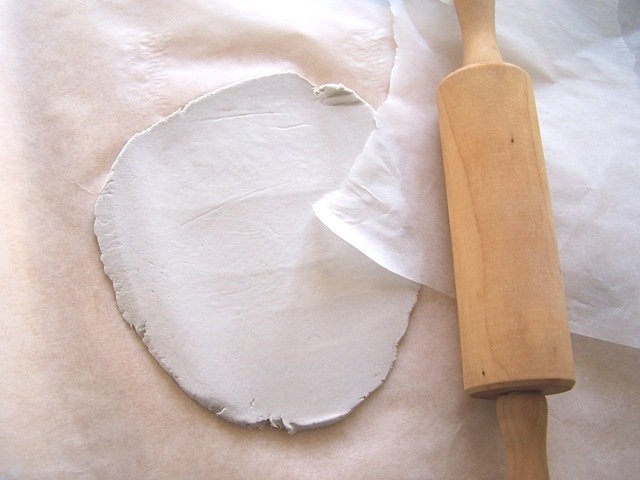 Prendete la pasta modellabile e mettetela tra due fogli di carta da forno. Spianatela con un matterello fino a creare uno strato di circa mezzo centimetro. Prendete la pasta modellabile e mettetela tra due fogli di carta da forno. Spianatela con un matterello fino a creare uno strato di circa mezzo centimetro.