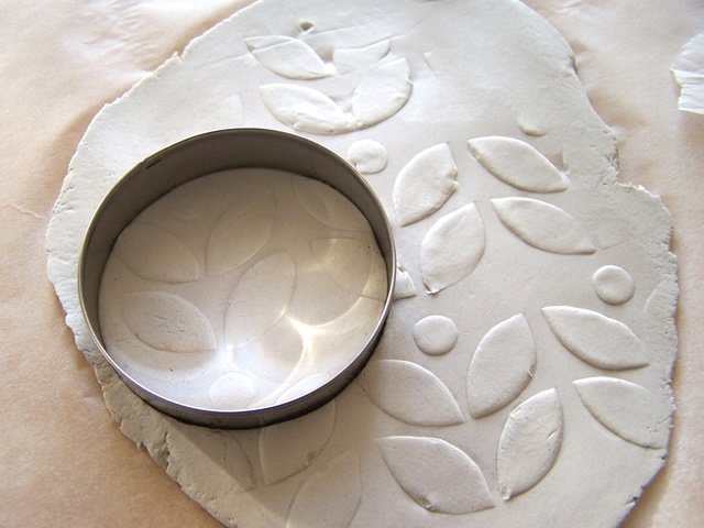 Rimuovere lentamente lo stencil e realizzate dei dischi di varie dimensioni con le formine per biscotti. Passare un dito bagnato nell’acqua sul bordo di ogni disco per smussare i bordi. Rimuovere lentamente lo stencil e realizzate dei dischi di varie dimensioni con le formine per biscotti. Passare un dito bagnato nell’acqua sul bordo di ogni disco per smussare i bordi.