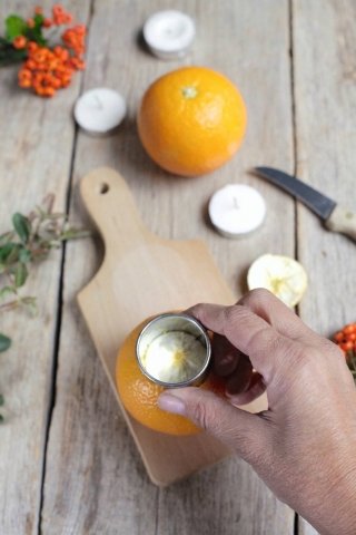 4. Dipingete l’asse di legno da posizionare sul tavolo con la vernice di colore arancione e fatela asciugare bene. Nel frattempo, incidete la calotta superiore delle arance utilizzando un coppapasta della misura del tealight, e inseritevi le candeline.