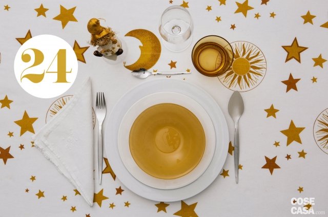 Stelle, lune, soli in oro su fondo bianco per chi sceglie una tovaglia di grande impatto estetico, perfetta in una casa con imbottiti bianchi, anche classici. I piatti saranno di linea contemporanea (la fondina è iridescente) come le posate e i bicchieri (quello per l’acqua è color oro). Un buffo omino con il cappello siede su una campanella beneaugurante. Stelle, lune, soli in oro su fondo bianco per chi sceglie una tovaglia di grande impatto estetico, perfetta in una casa con imbottiti bianchi, anche classici. I piatti saranno di linea contemporanea (la fondina è iridescente) come le posate e i bicchieri (quello per l’acqua è color oro). Un buffo omino con il cappello siede su una campanella beneaugurante.