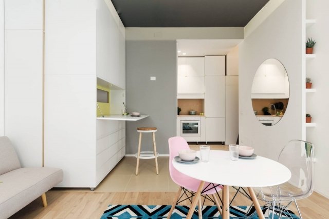 Lo spazio per cucinare e conservare il cibo, pur di dimensioni contenute, è concepito come un luogo funzionale dotato di tutto il necessario, non il semplice “angolo cottura” che solitamente contraddistingue i monolocali. Ogni centimetro disponibile è sfruttato, grazie alle armadiature su misura a tutta altezza laccate di bianco. Per la colazione o un pranzo veloce è predisposto anche un piano a ribalta nello schienale dell’armadiatura mobile adiacente. Il grande specchio circolare raddoppia la profondità spaziale e la luminosità. Lo spazio per cucinare e conservare il cibo, pur di dimensioni contenute, è concepito come un luogo funzionale dotato di tutto il necessario, non il semplice “angolo cottura” che solitamente contraddistingue i monolocali. Ogni centimetro disponibile è sfruttato, grazie alle armadiature su misura a tutta altezza laccate di bianco. Per la colazione o un pranzo veloce è predisposto anche un piano a ribalta nello schienale dell’armadiatura mobile adiacente. Il grande specchio circolare raddoppia la profondità spaziale e la luminosità.