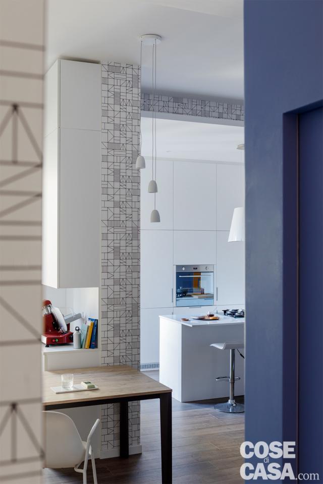 zona giorno con tavolo da pranzo, nicchia angolare, cucina in laccato bianco con penisola multifunzione. Finiture decorative in carta da parati a motivo geometrico zona giorno con tavolo da pranzo, nicchia angolare, cucina in laccato bianco con penisola multifunzione. Finiture decorative in carta da parati a motivo geometrico