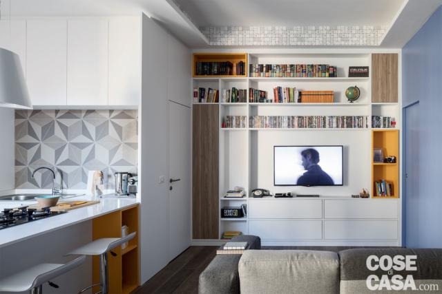 Parete attrezzata del soggiorno con vano tv, davanti al divano, con inserti in giallo e rovere, cucina con finiture decorative, porta filomuro della camera rifinita in bianco come il muro Parete attrezzata del soggiorno con vano tv, davanti al divano, con inserti in giallo e rovere, cucina con finiture decorative, porta filomuro della camera rifinita in bianco come il muro