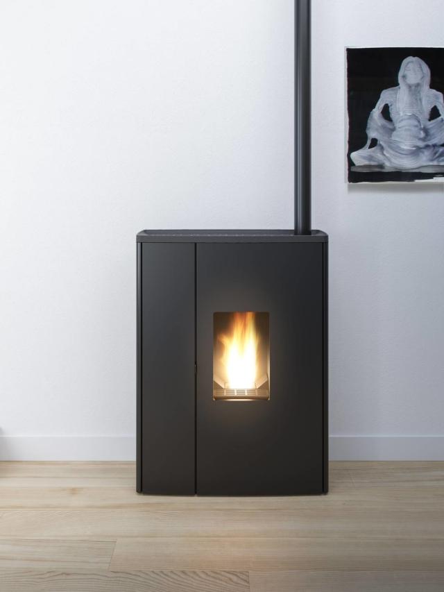 La stufa a pellet Doc, grazie allo scarico sul top, si può montare quasi a filo muro. Il rivestimento in acciaio nero riprende la finitura della canna fumaria. La stufa a pellet Doc, grazie allo scarico sul top, si può montare quasi a filo muro. Il rivestimento in acciaio nero riprende la finitura della canna fumaria.