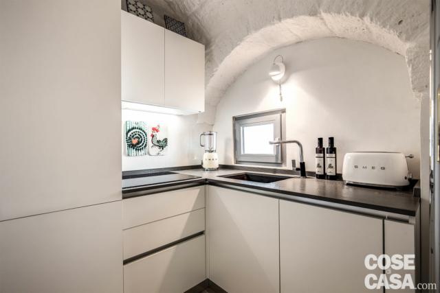 Nella rientranza creata dalla presenza della scala principale di accesso, dove già esisteva una cucina in muratura, è stato organizzato un piccolo vano per la preparazione e la cottura dei cibi. Il minimalismo della composizione Essebi, con finitura opaca bianca delle basi e dei pensili e top scuro, è sottolineato dalla matericità dell’arco strutturale di pietra a vista. E dalla poetica leggerezza della piccola applique Light Au Lait di Ingo Maurer, composta da tazza, piattino e cucchiaino. Nella rientranza creata dalla presenza della scala principale di accesso, dove già esisteva una cucina in muratura, è stato organizzato un piccolo vano per la preparazione e la cottura dei cibi. Il minimalismo della composizione Essebi, con finitura opaca bianca delle basi e dei pensili e top scuro, è sottolineato dalla matericità dell’arco strutturale di pietra a vista. E dalla poetica leggerezza della piccola applique Light Au Lait di Ingo Maurer, composta da tazza, piattino e cucchiaino.