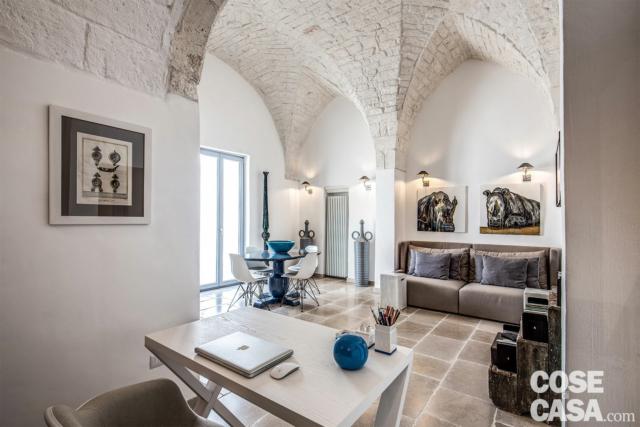 L’angolo conversazione nel soggiorno è risolto con un divanetto (Club di Musa) in nicchia e due materici tavolini di ceramica bianca InOut di Gervasoni, sovrastati da una coppia di quadri contemporanei. Qua e là, pezzi materici di provenienza locale (come le alte torciere ottocentesche) richiamano la tradizione pugliese. La portafinestra affacciata sulla loggia, così come tutti i serramenti dell’abitazione, è stata sostituita con un prodotto performante (Prolux Evolution di Oknoplast) dal punto di vista dell’isolamento e dell’esilità dei profili, per far entrare più luce possibile. L’angolo conversazione nel soggiorno è risolto con un divanetto (Club di Musa) in nicchia e due materici tavolini di ceramica bianca InOut di Gervasoni, sovrastati da una coppia di quadri contemporanei. Qua e là, pezzi materici di provenienza locale (come le alte torciere ottocentesche) richiamano la tradizione pugliese. La portafinestra affacciata sulla loggia, così come tutti i serramenti dell’abitazione, è stata sostituita con un prodotto performante (Prolux Evolution di Oknoplast) dal punto di vista dell’isolamento e dell’esilità dei profili, per far entrare più luce possibile.