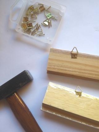 Sul retro delle cornici, attaccate gli agganci con chiodini e martello Sul retro delle cornici, attaccate gli agganci con chiodini e martello