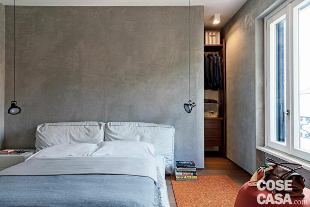 camera matrimoniale, parete grigia, letto tessile con testiera imbottita, faretti a sospensione, scendiletto rosso, finestra camera matrimoniale, parete grigia, letto tessile con testiera imbottita, faretti a sospensione, scendiletto rosso, finestra