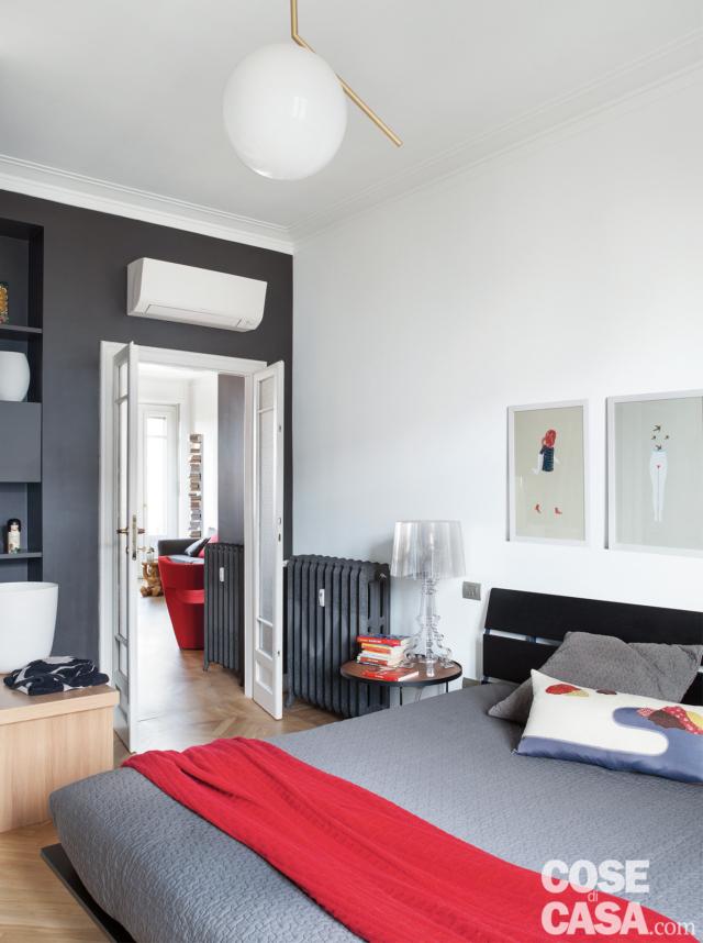 bilocale aperto, camera matrimoniale, letto con testiera a doghe, plaid rosso, radiatore in ghisa, lampada a sospensione di design, climatizzatore split, parete in finitura grigio scura bilocale aperto, camera matrimoniale, letto con testiera a doghe, plaid rosso, radiatore in ghisa, lampada a sospensione di design, climatizzatore split, parete in finitura grigio scura
