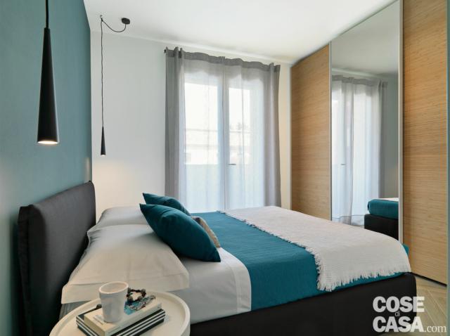camera matrimoniale, letto tessile, armadio con anta specchiata, portafinestra, sospensione conica, comodino, parete blu camera matrimoniale, letto tessile, armadio con anta specchiata, portafinestra, sospensione conica, comodino, parete blu