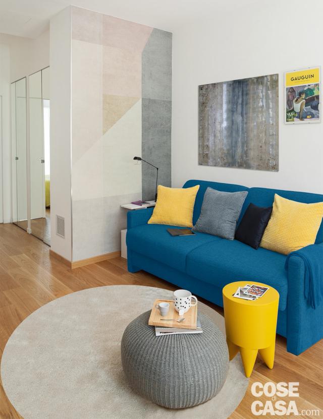 bilocale, zona conversazione, divano azzurro, cuscini gialli, pouf, tavolino, tappeto bianco, parete decorata con figure geometriche bilocale, zona conversazione, divano azzurro, cuscini gialli, pouf, tavolino, tappeto bianco, parete decorata con figure geometriche