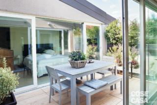 mansarda ristrutturata, terrazzino a tasca, tavolo da pranzo in legno con sedie e panchetta, vetrate scorrevoli, pavimento in teak, cameera matrimoniale, letto tessile con testiera imbottita