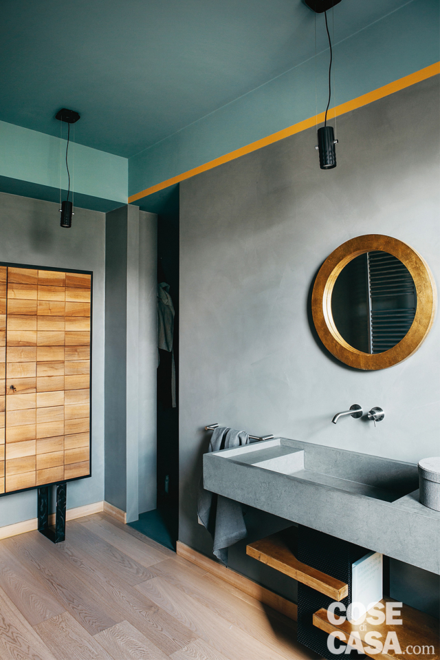 bagno dell'attico, lavabo sospeso in pietra naturale, specchio rotondo con cornice dorata, pareti grigie, pavimento in legno. mobile contenitore con cassetti in legno, soffitto azzurro bagno dell'attico, lavabo sospeso in pietra naturale, specchio rotondo con cornice dorata, pareti grigie, pavimento in legno. mobile contenitore con cassetti in legno, soffitto azzurro