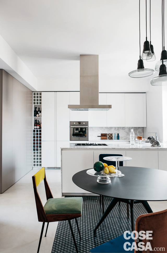 cucina dell'attico, composizione in laccato bianco opaco, cappa a isola, tavolo rotondo, sedie, inserto a pavimento in pietra lavica, lampade a sospensione cucina dell'attico, composizione in laccato bianco opaco, cappa a isola, tavolo rotondo, sedie, inserto a pavimento in pietra lavica, lampade a sospensione