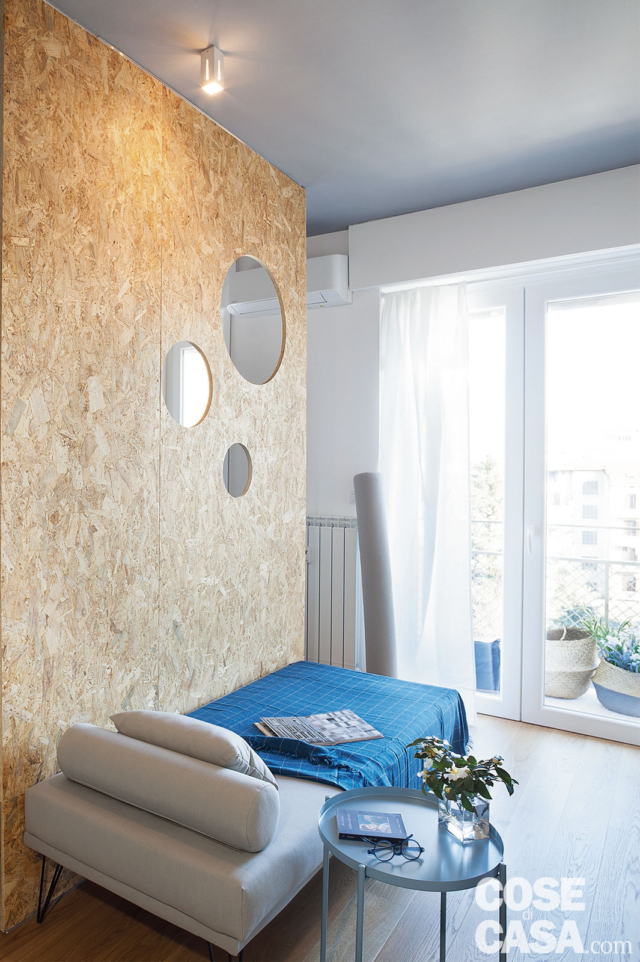 divano trasformato in letto, tavolino rotondo, parete in OSB con oblò, faretto, portafinestra divano trasformato in letto, tavolino rotondo, parete in OSB con oblò, faretto, portafinestra