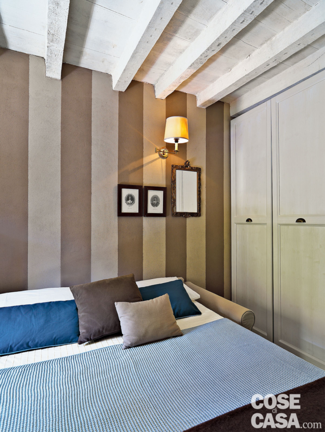 parete a righe, divano trasformato in letto, copriletto rigato, cuscini colorati, applique, armadio a muro, travi a vista parete a righe, divano trasformato in letto, copriletto rigato, cuscini colorati, applique, armadio a muro, travi a vista
