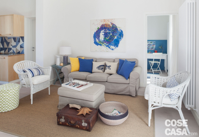 villa al mare, soggiorno, divano grigio, pouf, poltroncine in midollino bianco, tappeto écru, radiatore, baule, vaso villa al mare, soggiorno, divano grigio, pouf, poltroncine in midollino bianco, tappeto écru, radiatore, baule, vaso