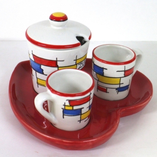 Il Set caffè con decoro Mondrian di Faetani Arte è in maiolica decorata a mano e cotta a 950 °C. Il vassoio a forma di cuore rosso ospita due tazzine e una zuccheriera. Il decoro Mondrian è realizzato a mano ed è stato rivisitato. Prezzo 46 euro. www.faetani.com
