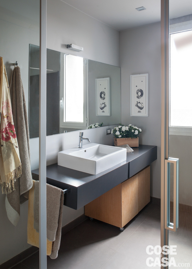 bagno del mini appartamento, mobile sospeso, lavabo da appoggio, specchiera, applique, finestra, pareti grigie, pavimento in resina bagno del mini appartamento, mobile sospeso, lavabo da appoggio, specchiera, applique, finestra, pareti grigie, pavimento in resina