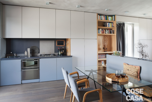 zona cottura, basi azzurre, pensili e colonne in laccato bianco opaco, libreria in rovere, tavolo da pranzo con piano in cristallo trasparente, sedie imbottite, parquet in rovere zona cottura, basi azzurre, pensili e colonne in laccato bianco opaco, libreria in rovere, tavolo da pranzo con piano in cristallo trasparente, sedie imbottite, parquet in rovere