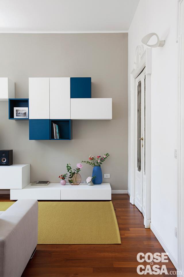 soggiorno del trilocale rinnovato, parete attrezzata, pensili bianchi e blu, tappeto color senape, parete grigia, applique, porta in legno e vetro, pavimento in parquet soggiorno del trilocale rinnovato, parete attrezzata, pensili bianchi e blu, tappeto color senape, parete grigia, applique, porta in legno e vetro, pavimento in parquet