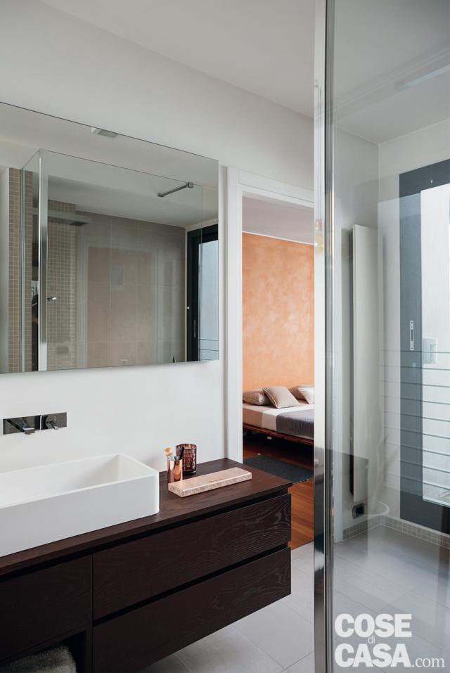 Nel bagno, il lavabo rettangolare con bordi smussati, appoggiato sul mobile sospeso in finitura wengé con cassetti frontali, è il modello Monolith di Casabath, la placca con il miscelatore a parete è di Gessi. Il pavimento è rivestito con piastrelle rettangolari in gres collezione Micron 2.0 di Imola Ceramica. Nel bagno, il lavabo rettangolare con bordi smussati, appoggiato sul mobile sospeso in finitura wengé con cassetti frontali, è il modello Monolith di Casabath, la placca con il miscelatore a parete è di Gessi. Il pavimento è rivestito con piastrelle rettangolari in gres collezione Micron 2.0 di Imola Ceramica.