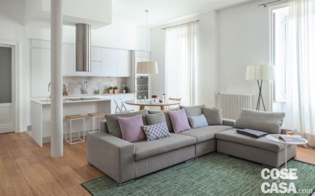 open space del bilocale moderno, divano con chaise longue in tessuto grigio, tappeto, portefinestre, pilastro, cucina, parquet open space del bilocale moderno, divano con chaise longue in tessuto grigio, tappeto, portefinestre, pilastro, cucina, parquet