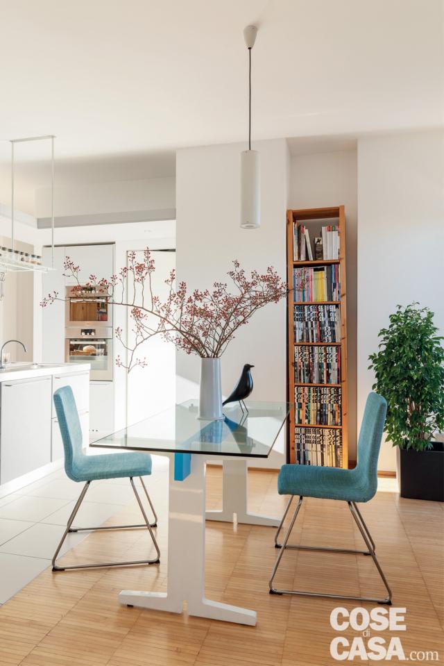 zona pranzo, tavolo con piano in vetro, sedie azzurre, libreria in nicchia, parquet industriale, cucina zona pranzo, tavolo con piano in vetro, sedie azzurre, libreria in nicchia, parquet industriale, cucina