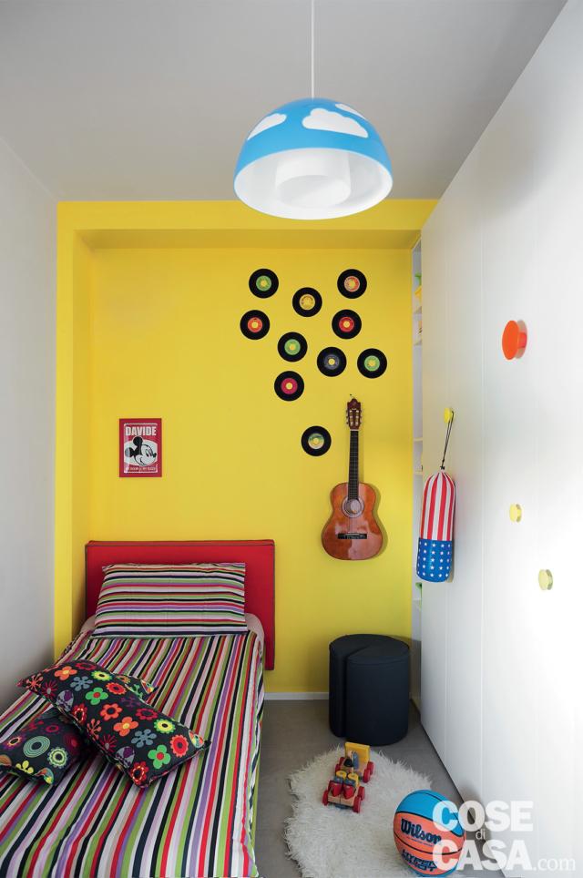 camera dei ragazzi, parete gialla, letto singolo, copriletto a righe, cuscini, chitarra appesa, tappeto, sospensione con diffusore azzurro decorato con nuvole camera dei ragazzi, parete gialla, letto singolo, copriletto a righe, cuscini, chitarra appesa, tappeto, sospensione con diffusore azzurro decorato con nuvole