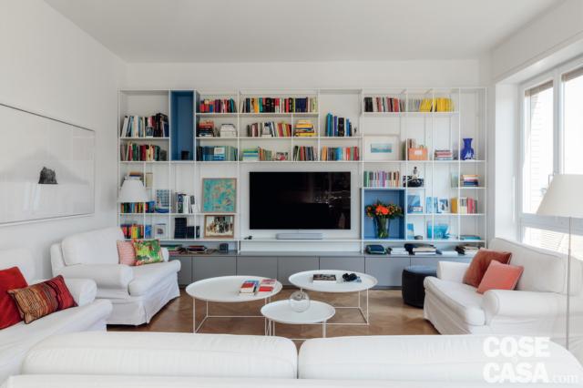 soggiorno dell'appartamento in centro, libreria a giorno bianca con zona tv, divani in tessuto bianco, tavolini rotondi, cuscini rossi, portafinestra, parquet in rovere, lampada da terra soggiorno dell'appartamento in centro, libreria a giorno bianca con zona tv, divani in tessuto bianco, tavolini rotondi, cuscini rossi, portafinestra, parquet in rovere, lampada da terra