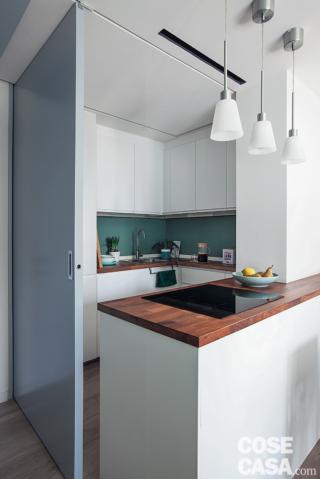 cucina, porta a battente azzurra, penisola con piano cottura a induzione, tre lampade a sospensione, pensili e basi in laccato bianco opaco, piani di lavoro color legno, controsoffitto cucina, porta a battente azzurra, penisola con piano cottura a induzione, tre lampade a sospensione, pensili e basi in laccato bianco opaco, piani di lavoro color legno, controsoffitto