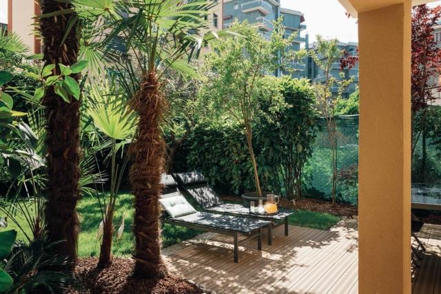 giardino interno, retro della casa su due livelli, palme, lettini, pavimento in legno, prato giardino interno, retro della casa su due livelli, palme, lettini, pavimento in legno, prato