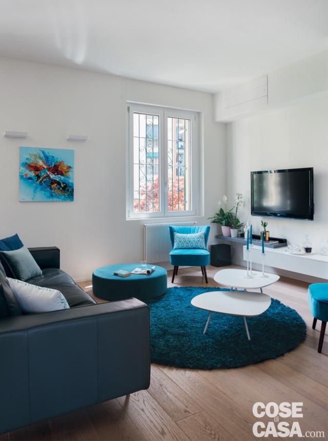 zona conversazione, mobile tv, poltroncina azzurra, finestra con inferriate, tappeto tondo, tavolino bianco con due piani sovrapposti, pavimento in legno, pouf e tappeto tondi, applique, divano in pelle zona conversazione, mobile tv, poltroncina azzurra, finestra con inferriate, tappeto tondo, tavolino bianco con due piani sovrapposti, pavimento in legno, pouf e tappeto tondi, applique, divano in pelle