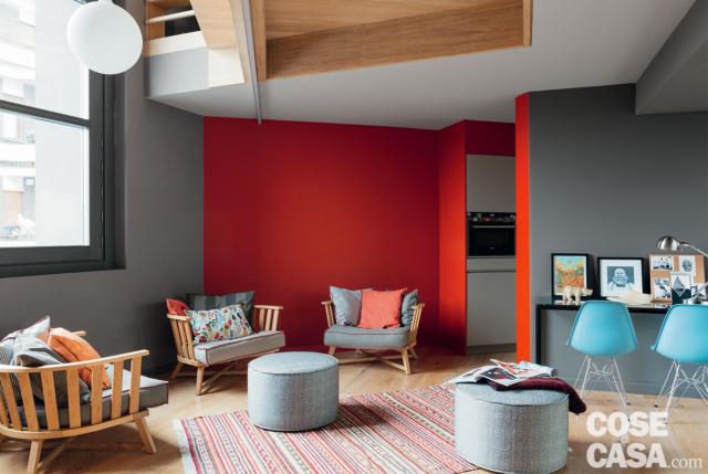 soggiorno del loft su due quote, poltroncine in legno, pouf rotondi, tappeto rigato, consolle, sedie azzurre, parete rossa, ingresso della cucina soggiorno del loft su due quote, poltroncine in legno, pouf rotondi, tappeto rigato, consolle, sedie azzurre, parete rossa, ingresso della cucina