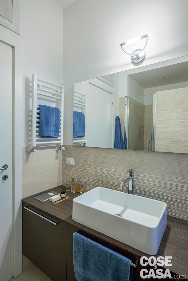 bagno, rivestimento a parete con texture in rilievo, mobile in legno tinto scuro, lavabo da appoggio in ceramica, miscelatore in acciaio cromato, specchio, applique, scaldasalviette bianco bagno, rivestimento a parete con texture in rilievo, mobile in legno tinto scuro, lavabo da appoggio in ceramica, miscelatore in acciaio cromato, specchio, applique, scaldasalviette bianco