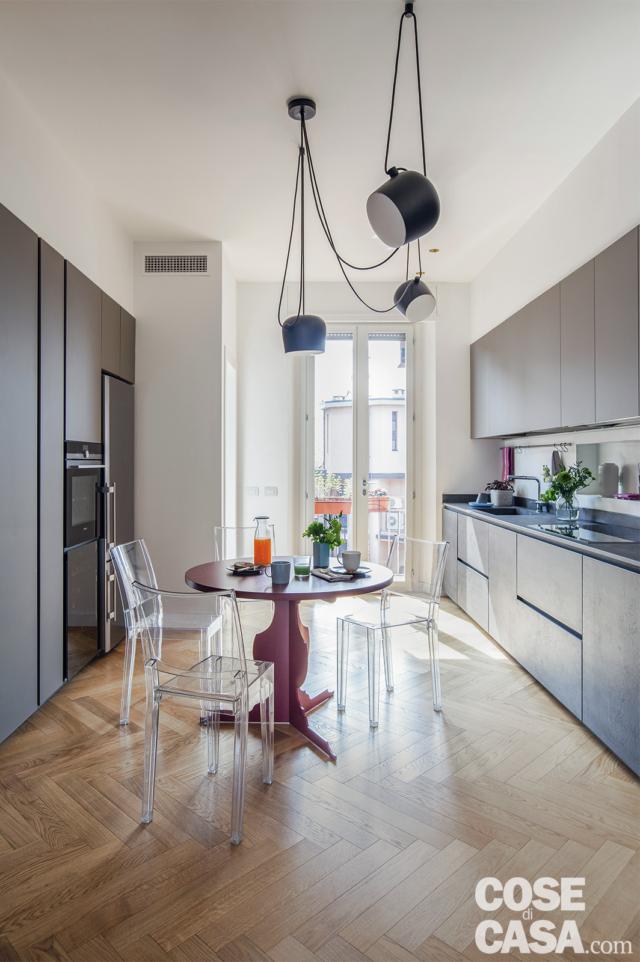 cucina. composizione su due lati in finitura antracite, colonne, basi e pensili, tavolo rotondo rosso, sedie trasparenti, lampada di design, parquet a spina di pesce cucina. composizione su due lati in finitura antracite, colonne, basi e pensili, tavolo rotondo rosso, sedie trasparenti, lampada di design, parquet a spina di pesce
