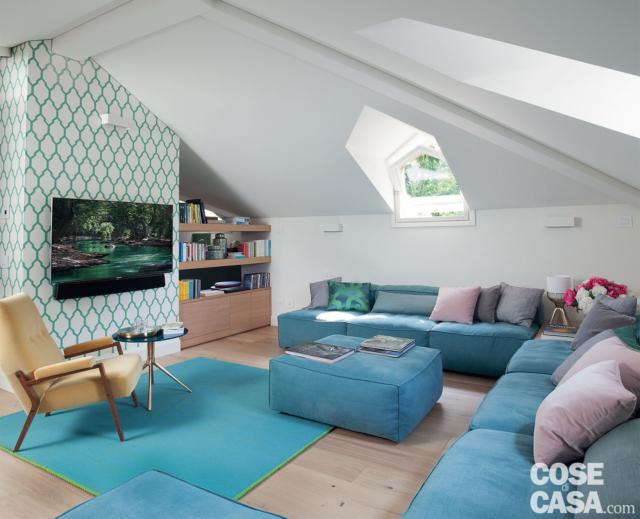 soggiorno della mansarda ristrutturata, divano angolare azzurro, finestra ad abbaino, pouf azzurro, carata da parati bianca e verde, tv, poltroncina vintage, tavolino rotondo, ripiani nel sottotetto soggiorno della mansarda ristrutturata, divano angolare azzurro, finestra ad abbaino, pouf azzurro, carata da parati bianca e verde, tv, poltroncina vintage, tavolino rotondo, ripiani nel sottotetto