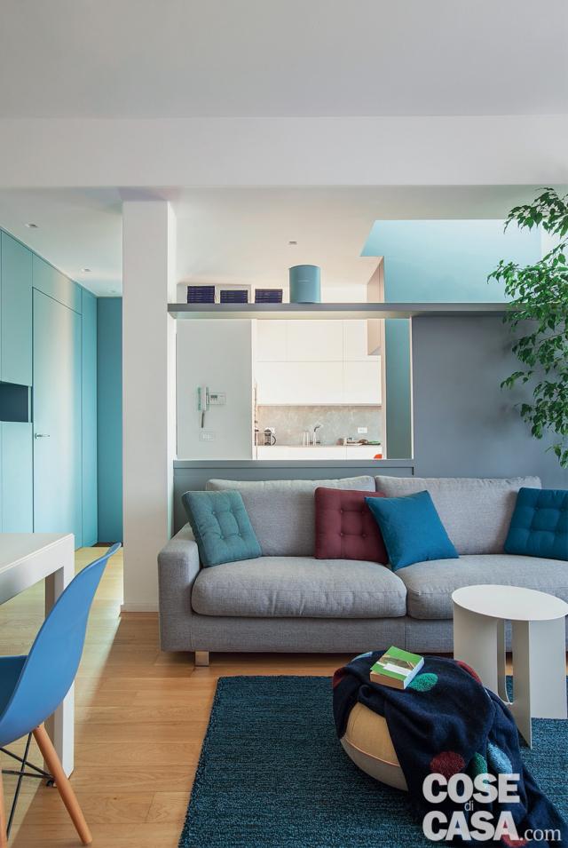 zona giorno del sottotetto su due livelli, divano grigio, cuscini trapuntati, tavolino bianco, pouf, tappeto, mobile su disegno con porta rasomuro integrata, pilastro, parete divisoria zona giorno del sottotetto su due livelli, divano grigio, cuscini trapuntati, tavolino bianco, pouf, tappeto, mobile su disegno con porta rasomuro integrata, pilastro, parete divisoria