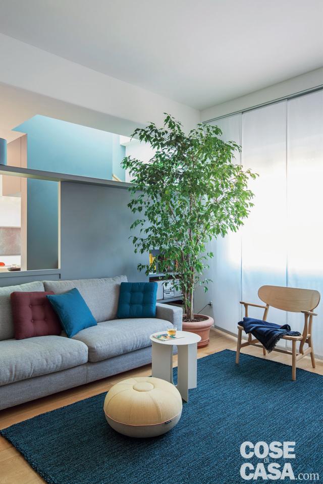 zona conversazione, dettagli, divano grigio, cuscini trapuntati, poltroncina di legno, pouf, tappeto color petrolio, tavolino bianco, tende a pannello, parete divisoria zona conversazione, dettagli, divano grigio, cuscini trapuntati, poltroncina di legno, pouf, tappeto color petrolio, tavolino bianco, tende a pannello, parete divisoria